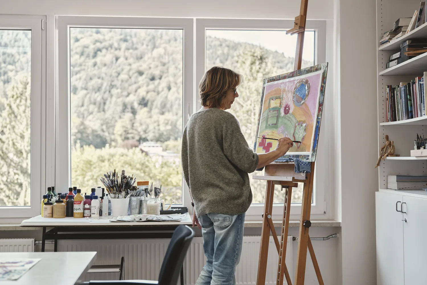 Frau malt an einer Staffelei im hellen Atelier der Kunsttherapie