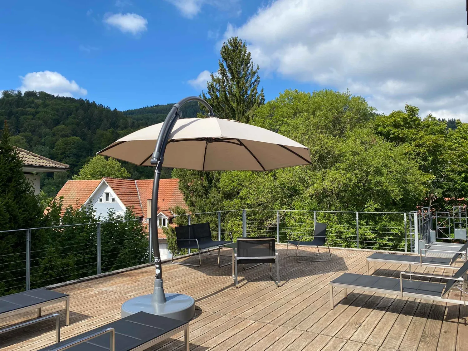 Sonnenterrasse mit Liegen und Sonnenschirm vor bewaldetem Hang